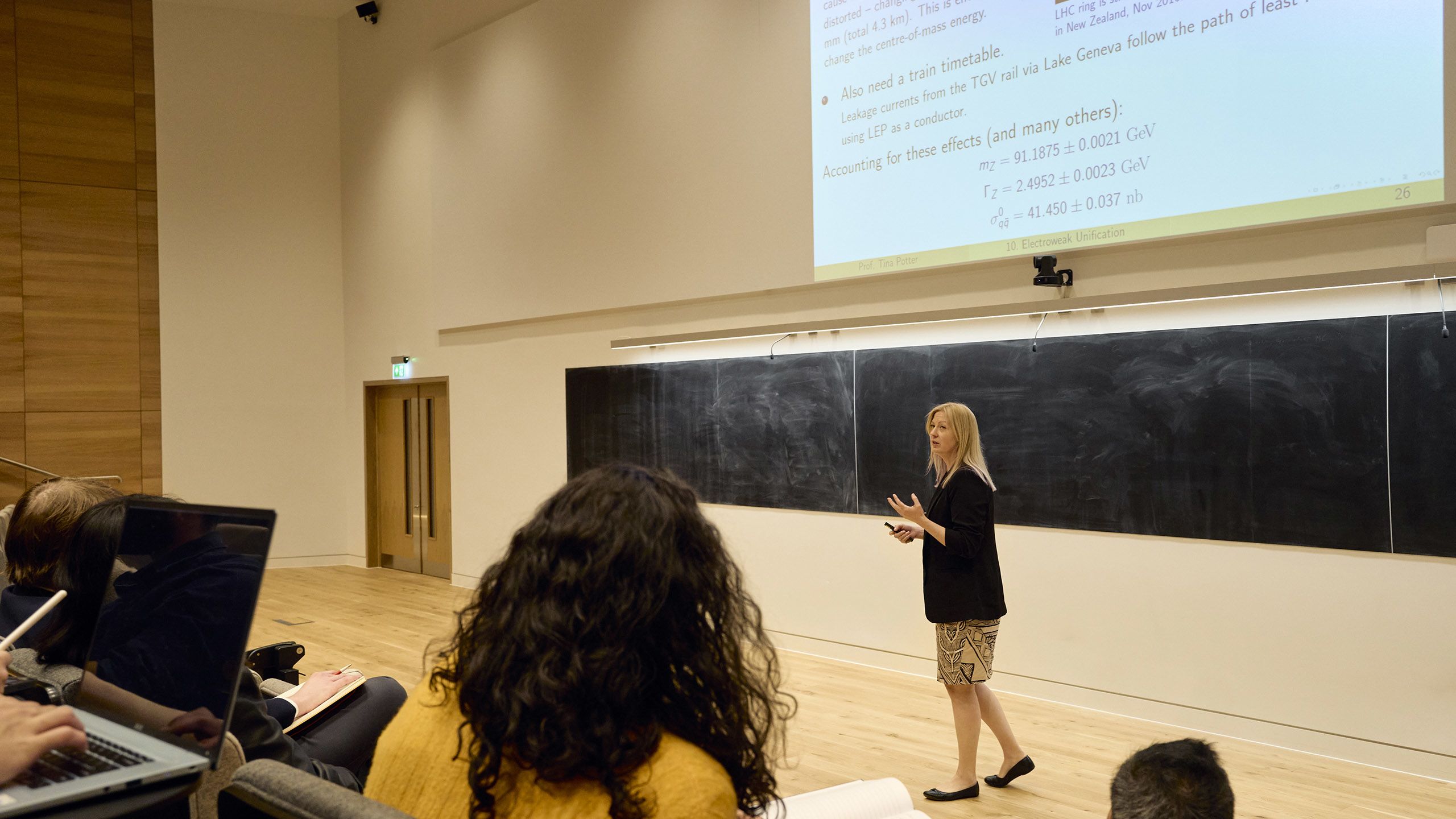 Professor Tina Potter gives a university lecture in front of a large blackboard and electronic screen