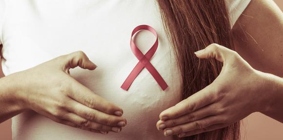 Breast cancer. Female hands make heart on pink ribbon