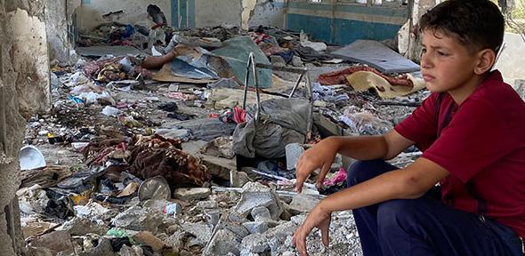 Boy sitting in the rubble of a destroyed UNRWA school in Nuseirat, Middle Areas, Gaza 2024
