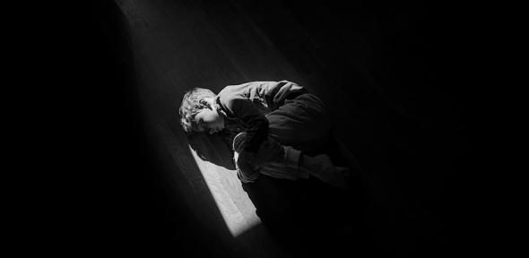 Black and white image of boy curled up on the floor