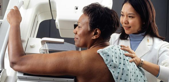 Female doctor standing near woman patient doing breast cancer scan