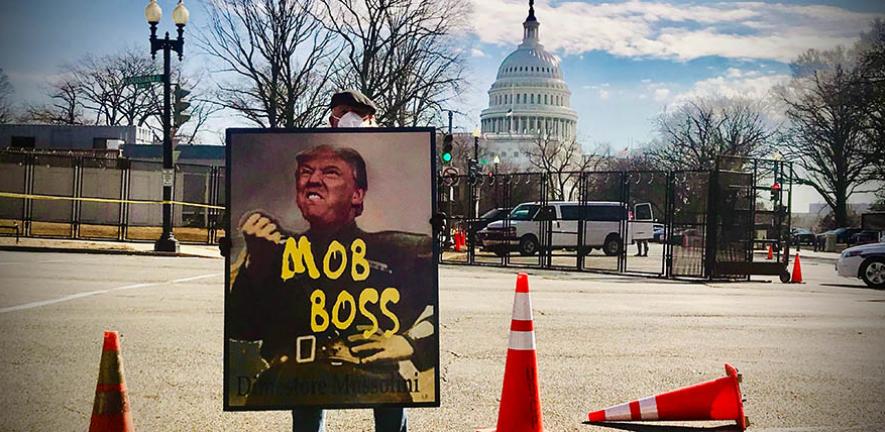 A protester holds a sign comparing President Trump to Italian dictator Benito Mussolini.