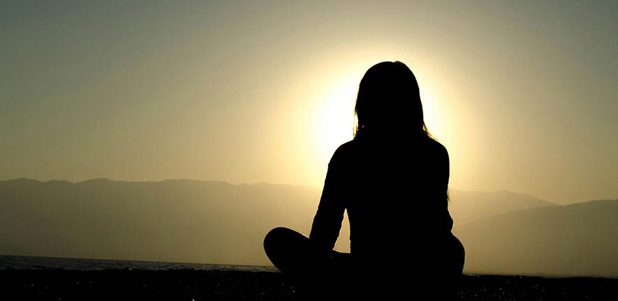 Woman sitting on sand at sunset meditating