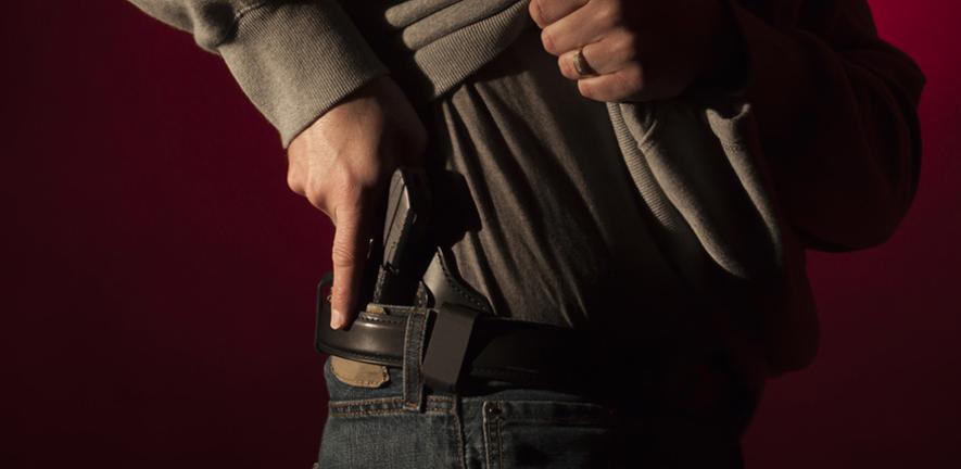 A man drawing a conceal carry pistol from an inside the waistband holster