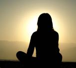 Woman sitting on sand at sunset meditating