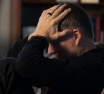 A man sitting on a couch holding his head in his hands