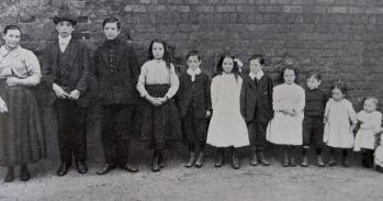 Black and white photograph of a family lined up against a wall, taken from a report on the physical welfare of mothers and children.