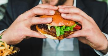 Person holding burger bun with vegetables and meat