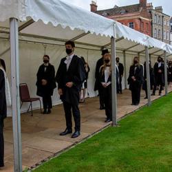 Graduands in academic dress for graduation standing in a socially distanced queue wearing masks