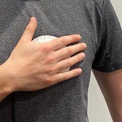 Person wearing a grey t-shirt holding a palm-sized device to their chest