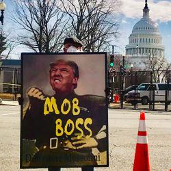 A protester holds a sign comparing President Trump to Italian dictator Benito Mussolini.