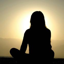 Woman sitting on sand at sunset meditating