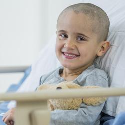 A little boy with a shaved head is smiling as he is laying on a hospital bed.
