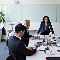 Businesswoman interacting with colleagues sitting at conference table during meeting in board room - stock photo
