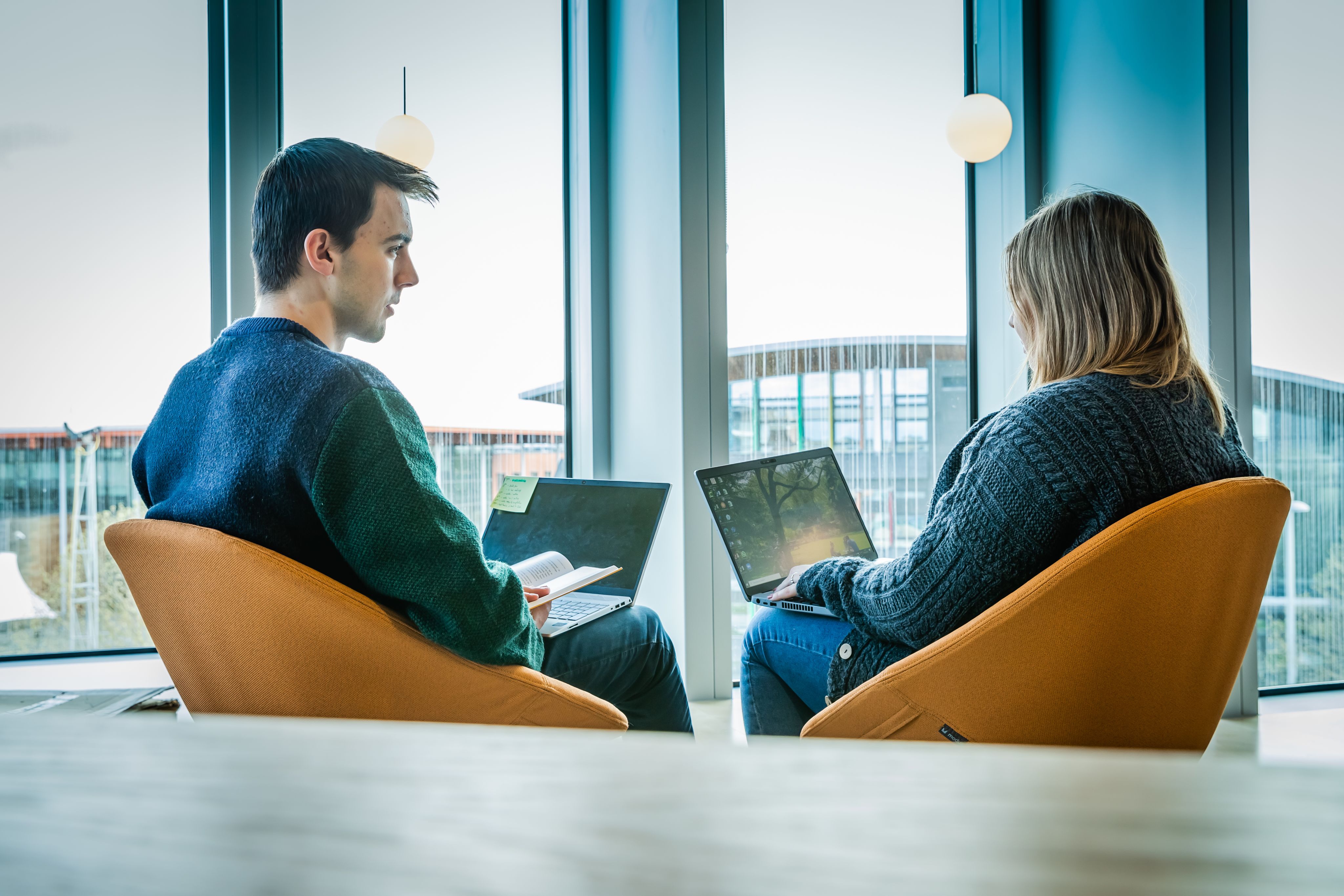 Two people talking to one another with laptops on their knee