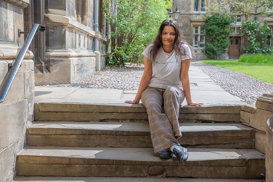 Ashna Biju in the grounds of Caius College, sitting on stone steps