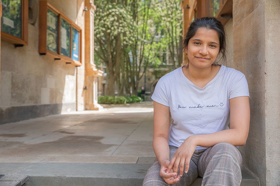 Ashna Biju in the grounds of Caius College, sitting in stone passage