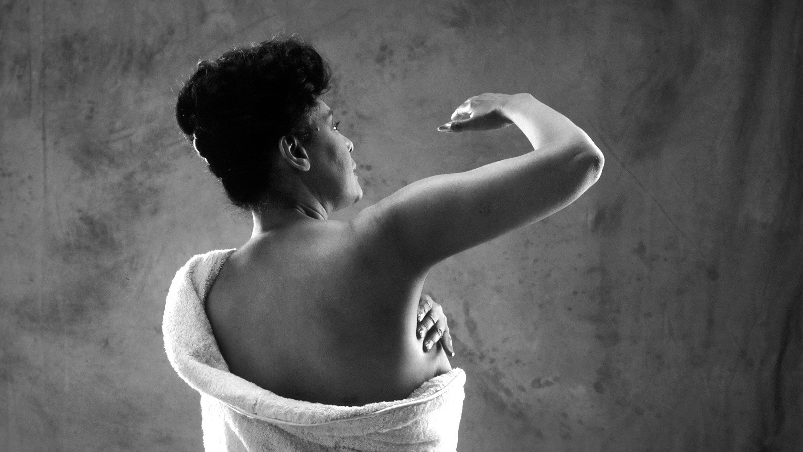 Woman wrapped in white towel checking her breast for signs of cancer