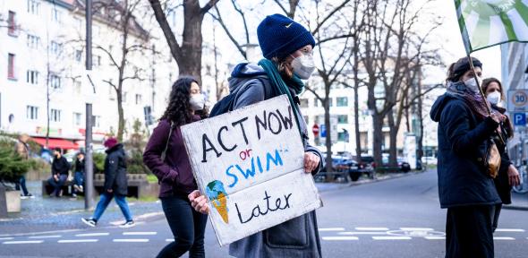 A man holds a sign that says 'Act now or swim later'