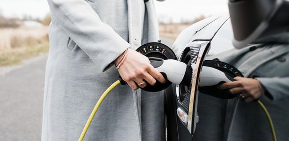 View of woman's hand plugging in charging lead to her electric car