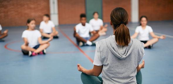 Rear view of sports teacher practicing Yoga with her students at school gym