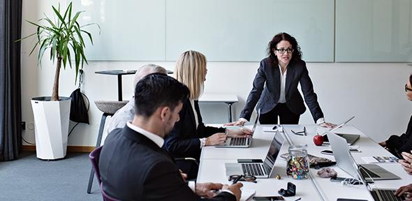 Businesswoman interacting with colleagues sitting at conference table during meeting in board room - stock photo