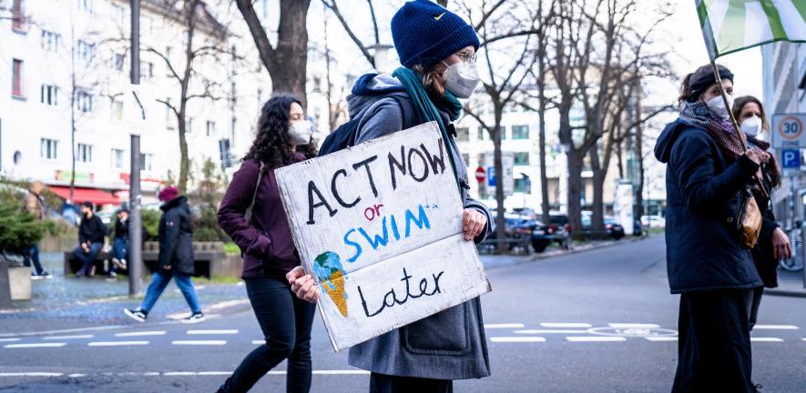 A man holds a sign that says 'Act now or swim later'