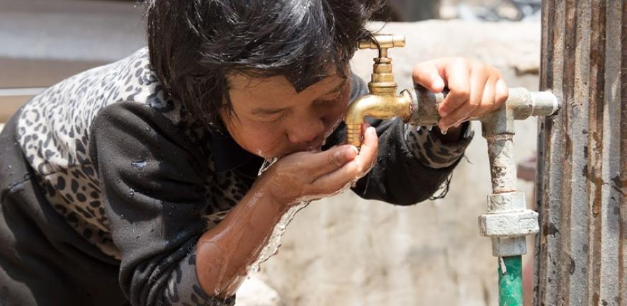 A young child drinks from a water tap