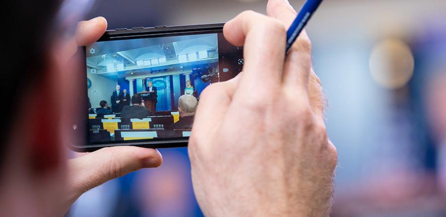 A reporter takes a photo of Donald Trump during a White House coronavirus briefing in April