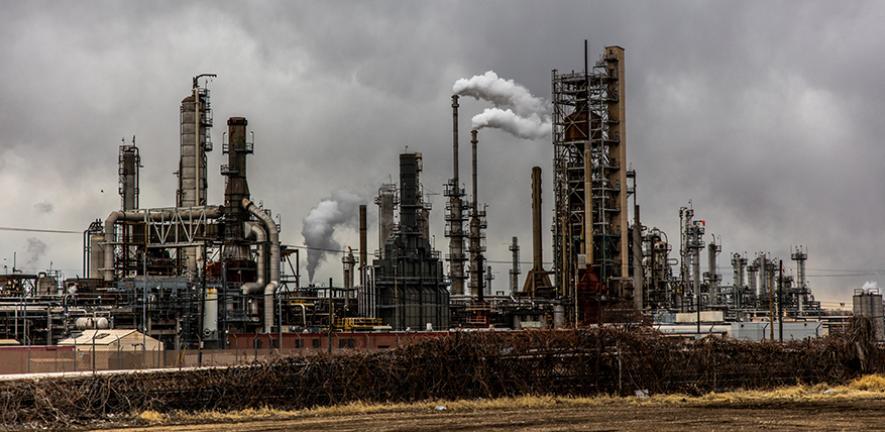 Factories with smoke under cloudy sky