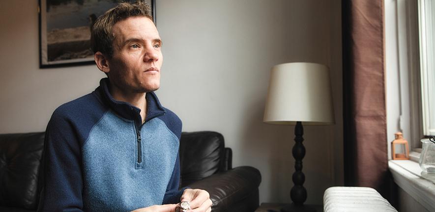 Autistic trans man at home looking out of a window