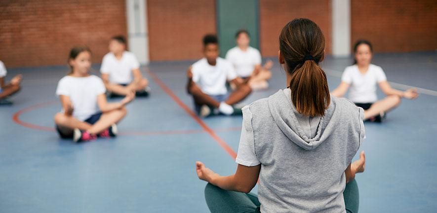 Rear view of sports teacher practicing Yoga with her students at school gym