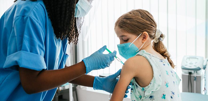 Young girl watching herself being injected with COVID-19 vaccine at a medical clinic