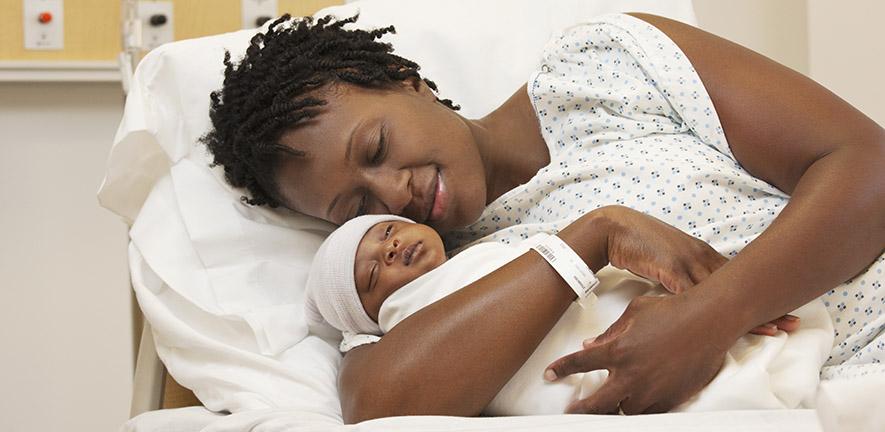 Black woman holding newborn baby in hospital bed