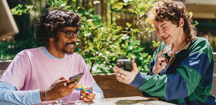 Two autistic friends sitting outside using stim toys and laughing at their phones