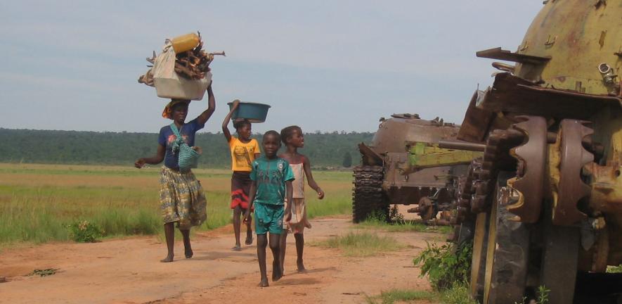 Angolan civilians walking past the remains of tanks in 2004. Relics of the conflict still litter the Angolan countryside.