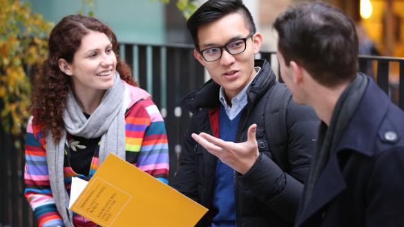 Three students chatting with a text book