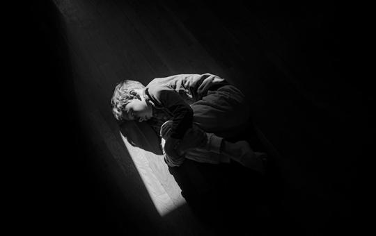 Black and white image of boy curled up on the floor