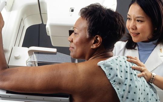 Female doctor standing near woman patient doing breast cancer scan