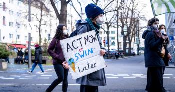 A man holds a sign that says 'Act now or swim later'