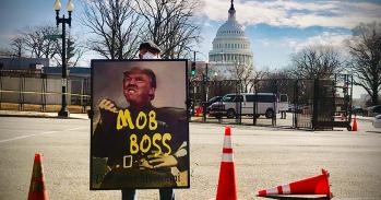 A protester holds a sign comparing President Trump to Italian dictator Benito Mussolini.