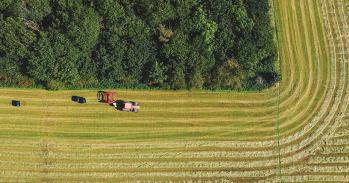 Drone view of agricultural field - a tractor is baling hay next to woodland