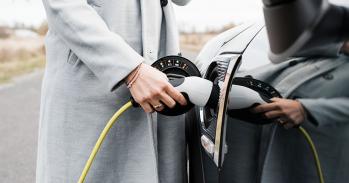 View of woman's hand plugging in charging lead to her electric car