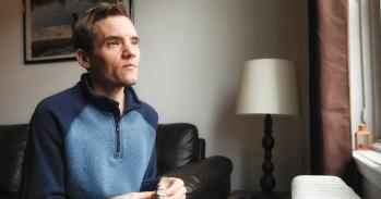 Autistic trans man at home looking out of a window 