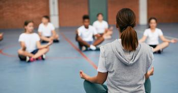 Rear view of sports teacher practicing Yoga with her students at school gym