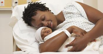 Black woman holding newborn baby in hospital bed